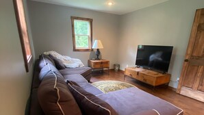 A modern living room with a brown sofa, a wooden TV stand, a lamp, and a window.