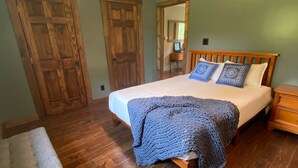 A bedroom with a wooden bed, a bench, a ceiling fan, and wooden flooring.