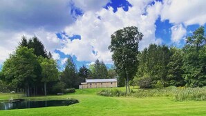 A grassy area with a pond, trees, and a building in the background.