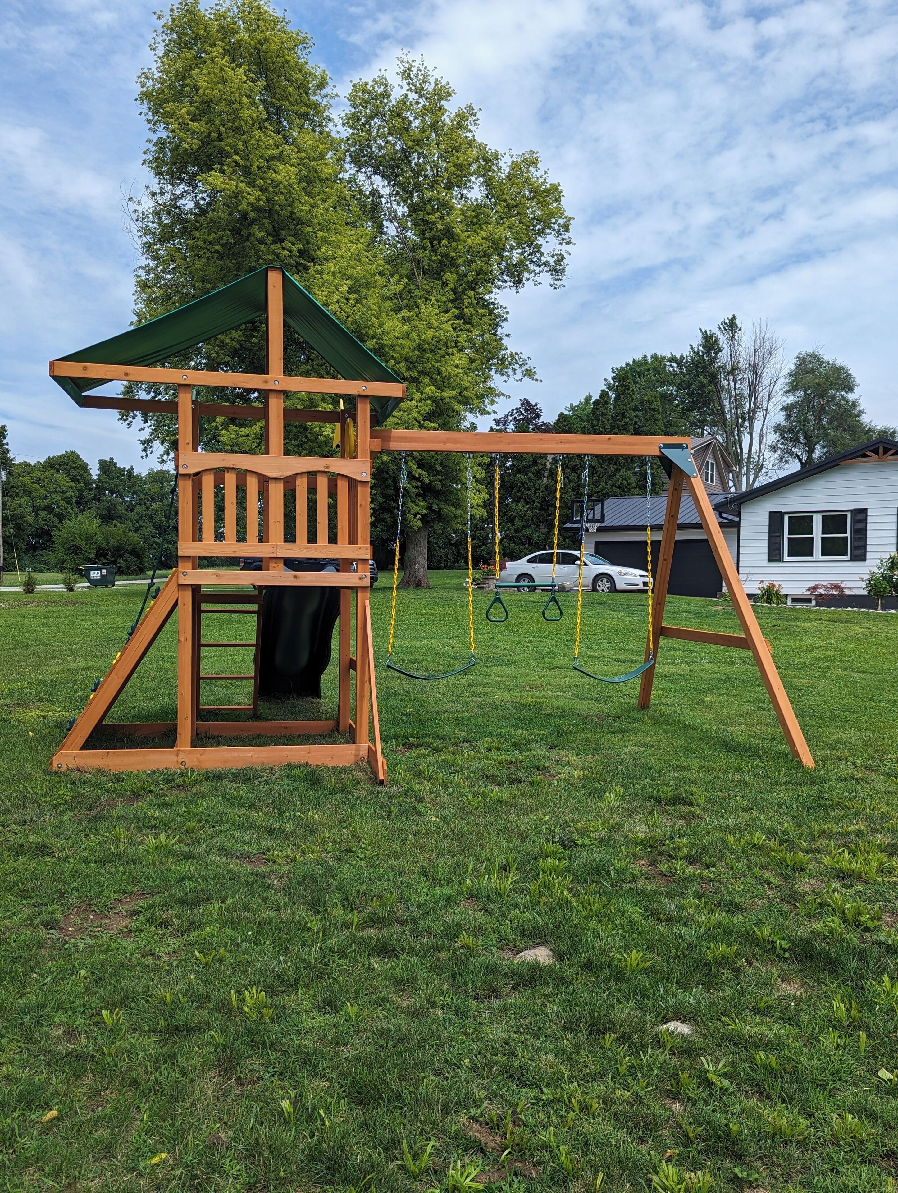 A wooden play structure with a climbing wall and swings in a grassy yard.