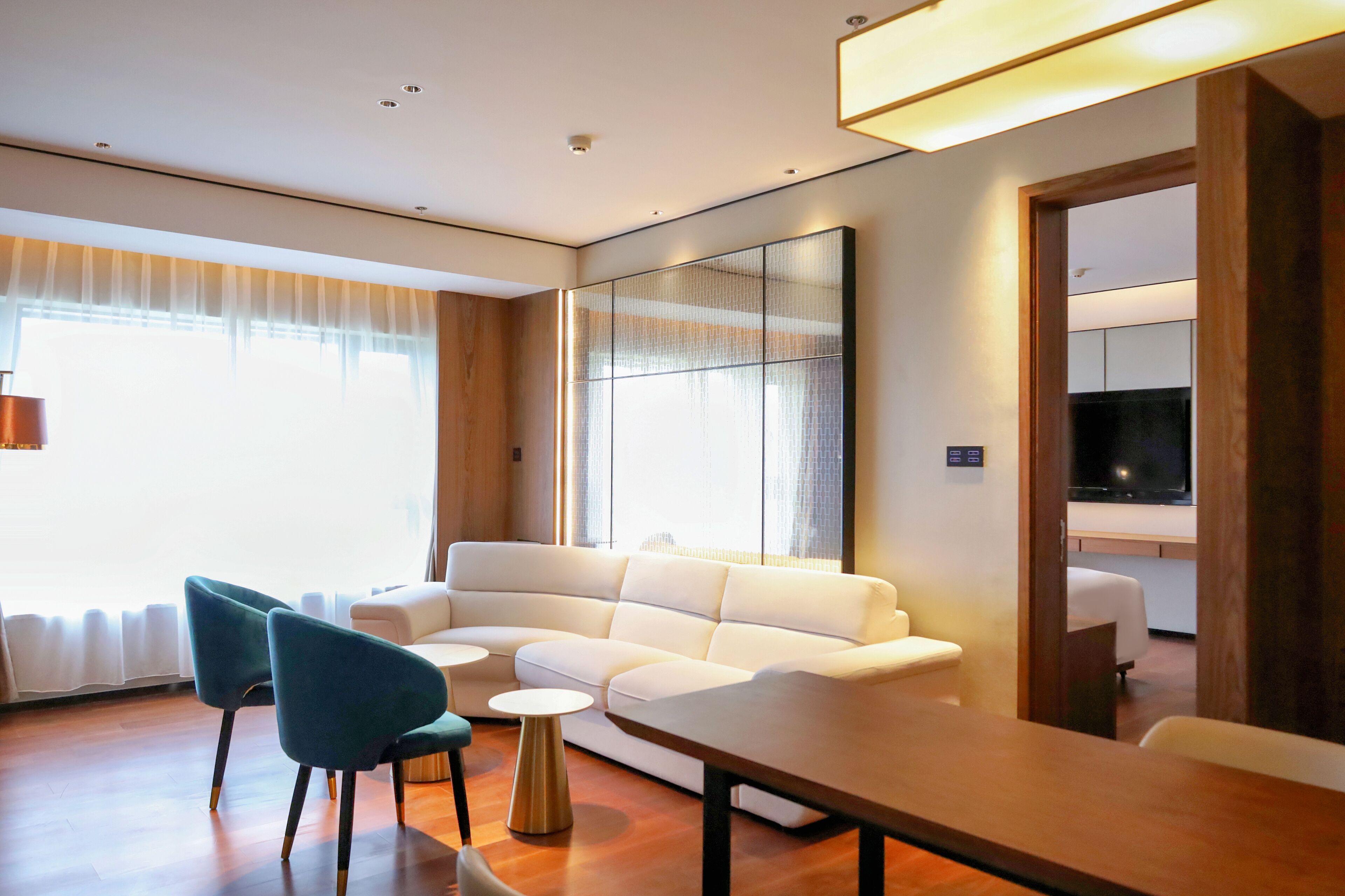 Ein modernes Wohnzimmer mit einem weißen Sofa, türkisfarbenen Sesseln, einem Holztisch und einem großen Spiegel an der Wand.