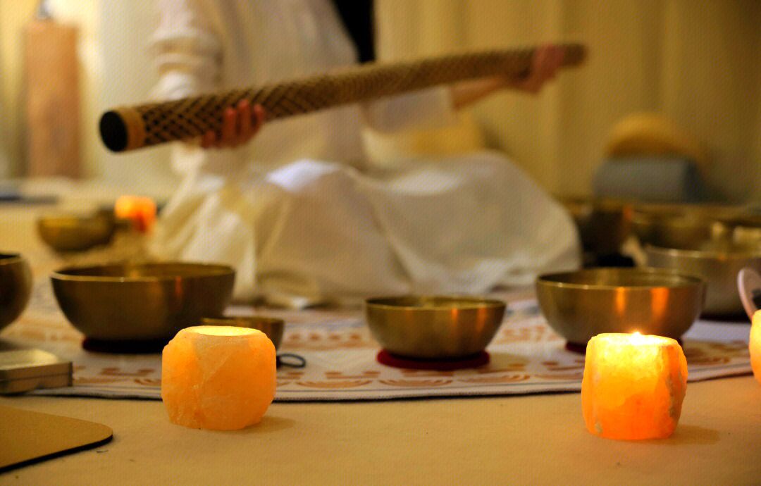 A person in white robes holding a drum, surrounded by several bowls and candles on a table.