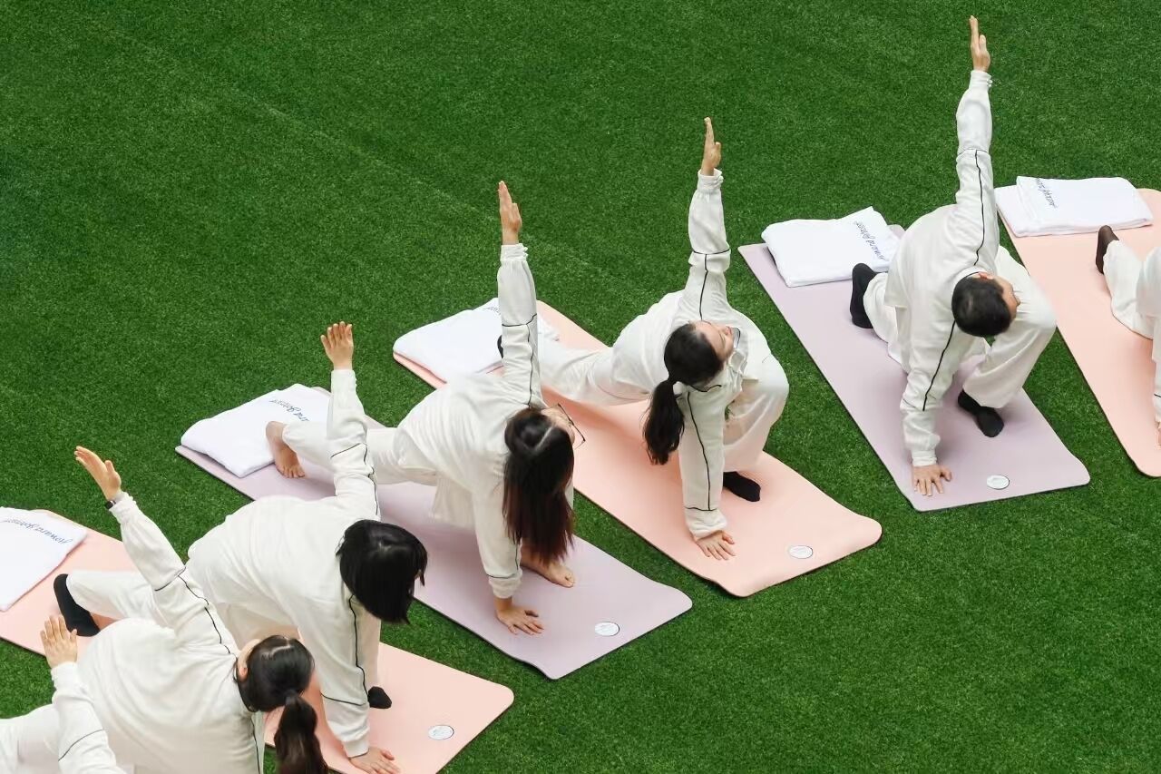Un grupo de personas practicando yoga sobre esterillas dispuestas en círculo en un campo cubierto de hierba.