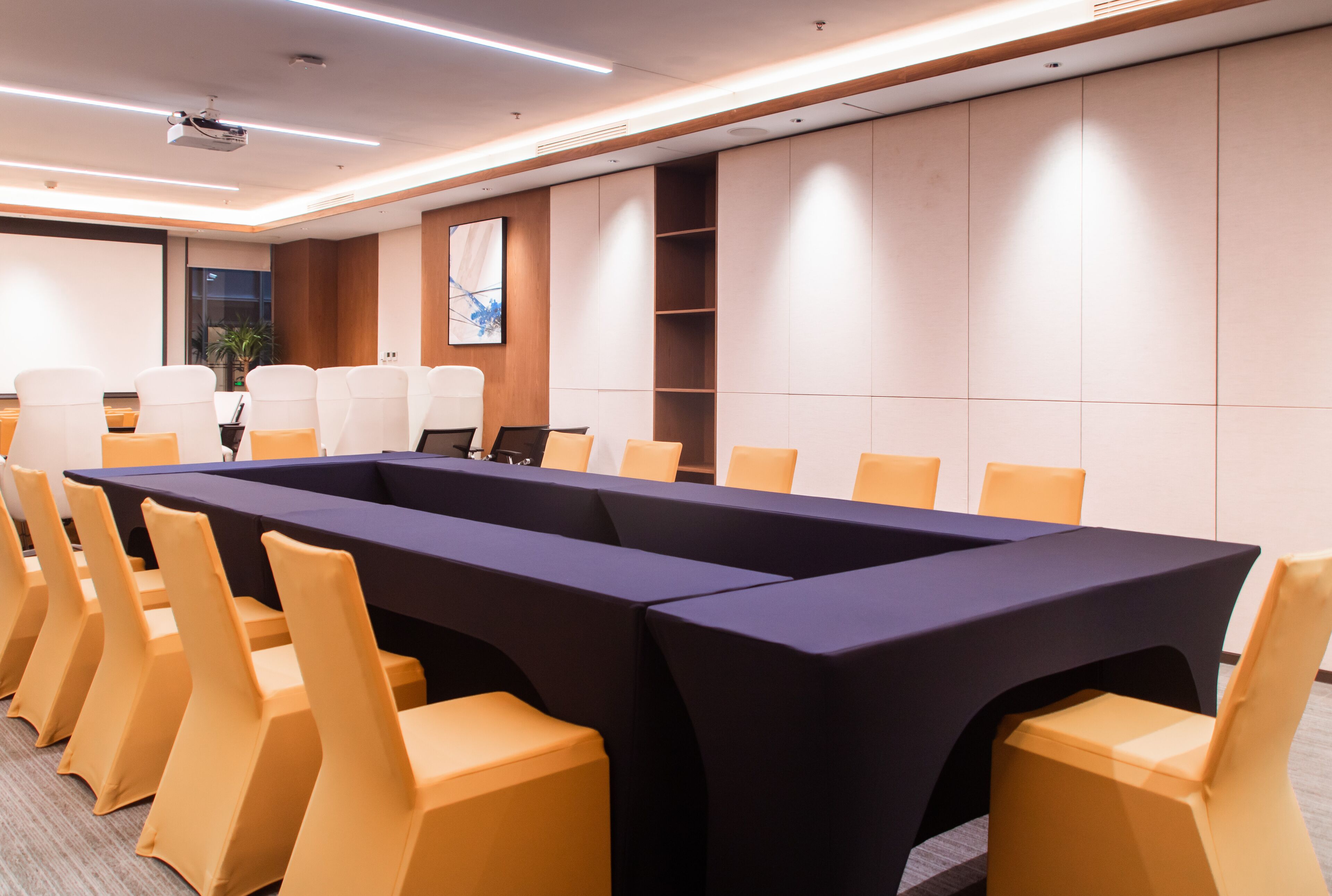 A conference room with a long table and chairs, a projector, and a large window.