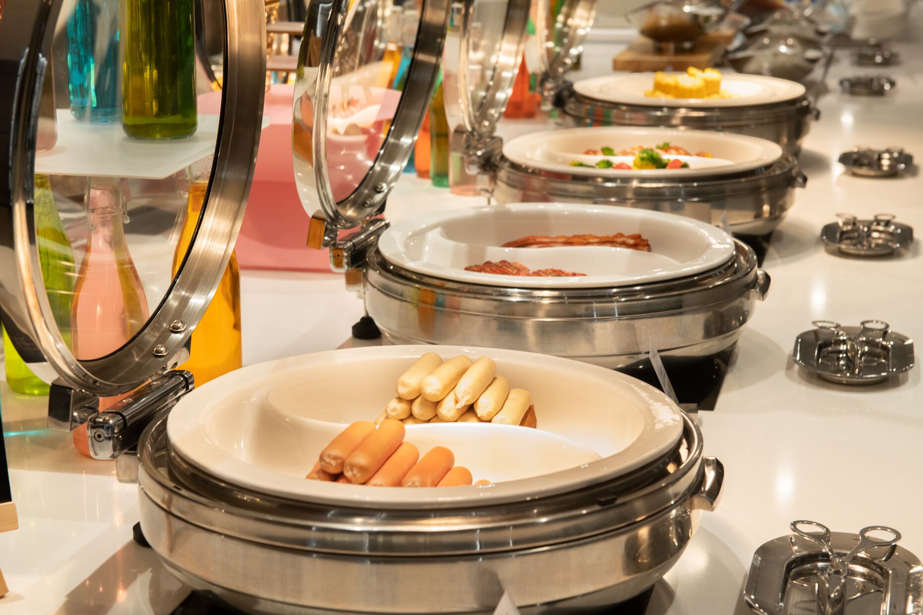 A buffet setup with multiple serving stations, each with a covered dish and utensils.