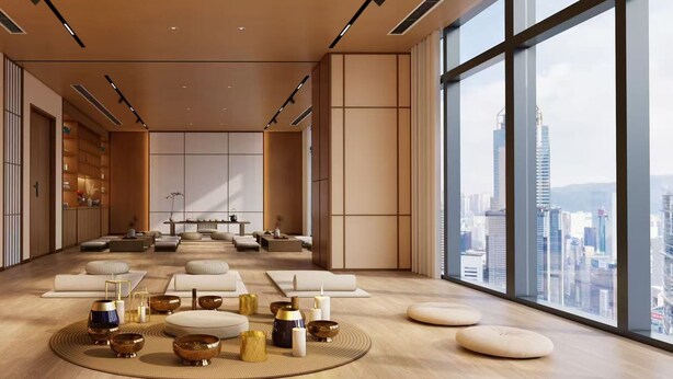 Amplia habitación con vista a la ciudad, que cuenta con una zona de estar central con cojines y una mesa baja, sobre un suelo de madera y frente a grandes ventanales.