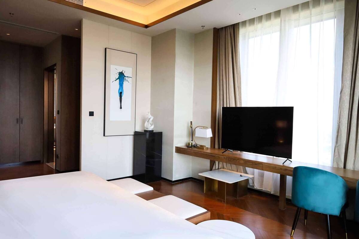 Une chambre d’hôtel moderne dotée d’un grand lit, d’un bureau avec un téléviseur à écran plat, d’une petite table et d’une chaise.