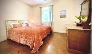 Un dormitorio con una cama, un aparador, una ventana con cortinas y un pequeño cuadro en la pared.