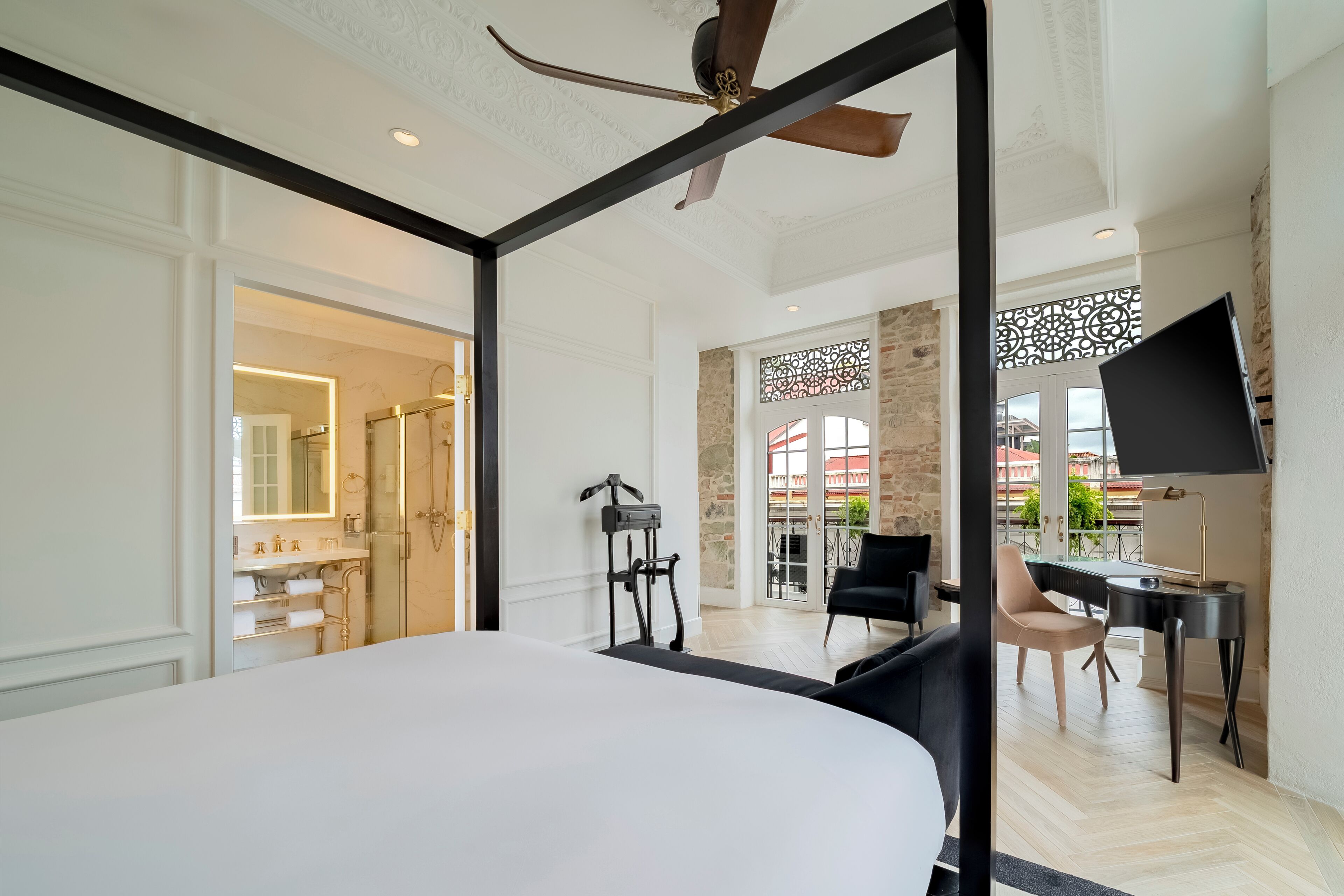 Una habitación de hotel moderna con una cama grande, un escritorio y una silla. Cuenta con ventilador de techo, televisión y vistas al exterior.