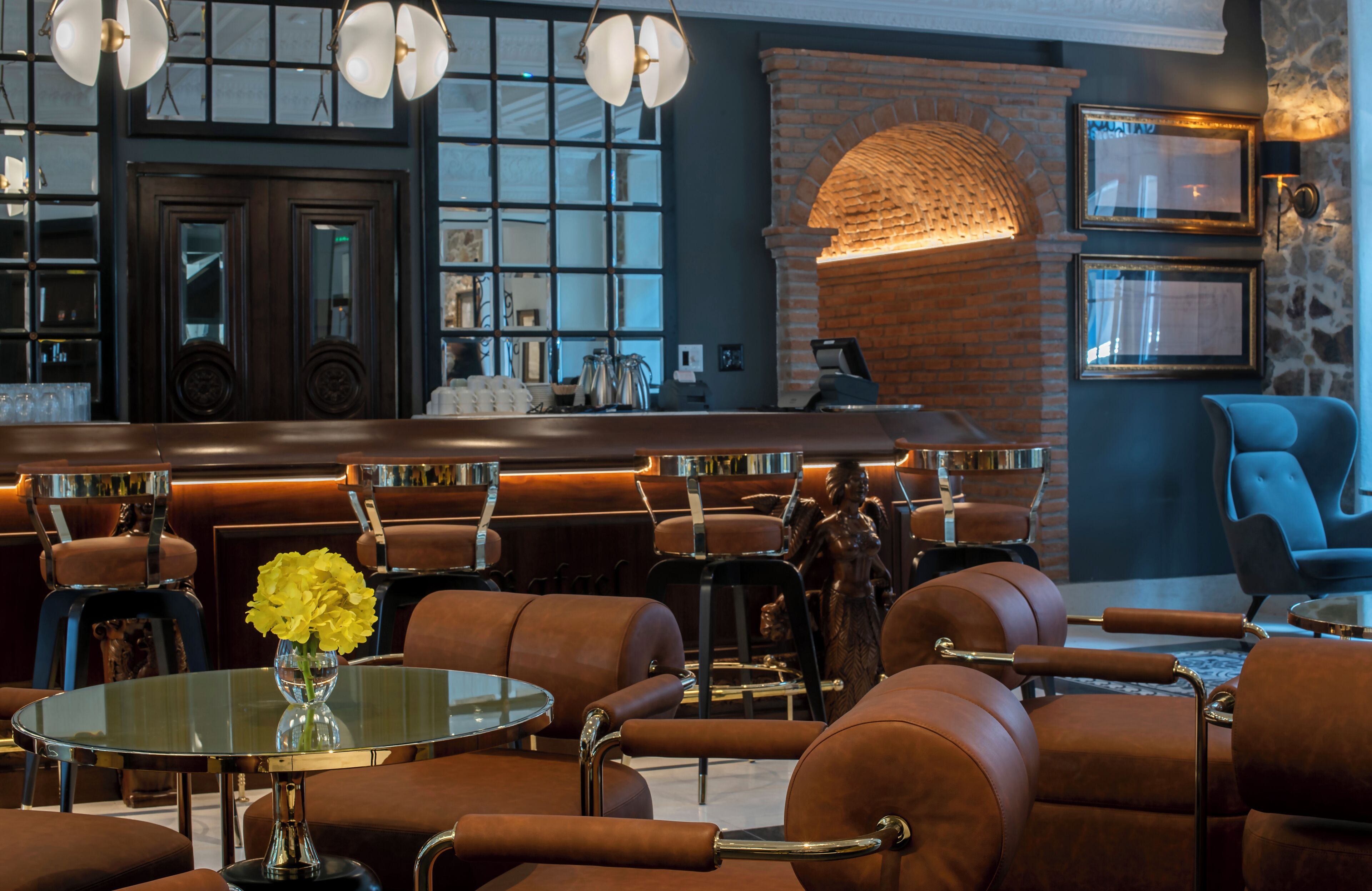 Een bar met lederen zitplaatsen, een glazen tafel met een bloevas en een haard van baksteen.