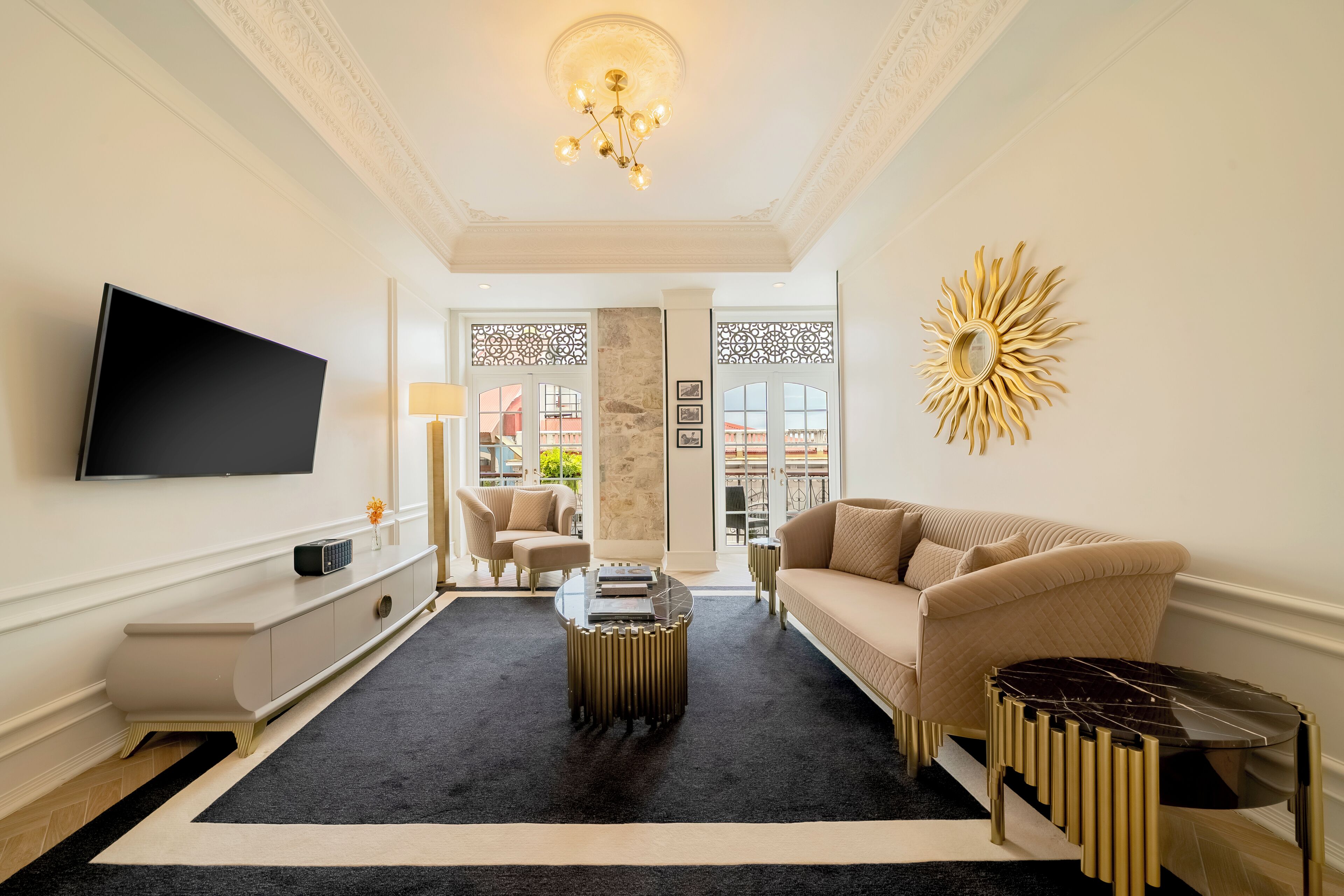 A modern living room with a flat-screen TV, a beige sofa, a coffee table, and a decorative sun-like wall piece.