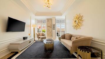 A modern living room with a flat-screen TV, a beige sofa, a coffee table, and a decorative sun-like wall piece.