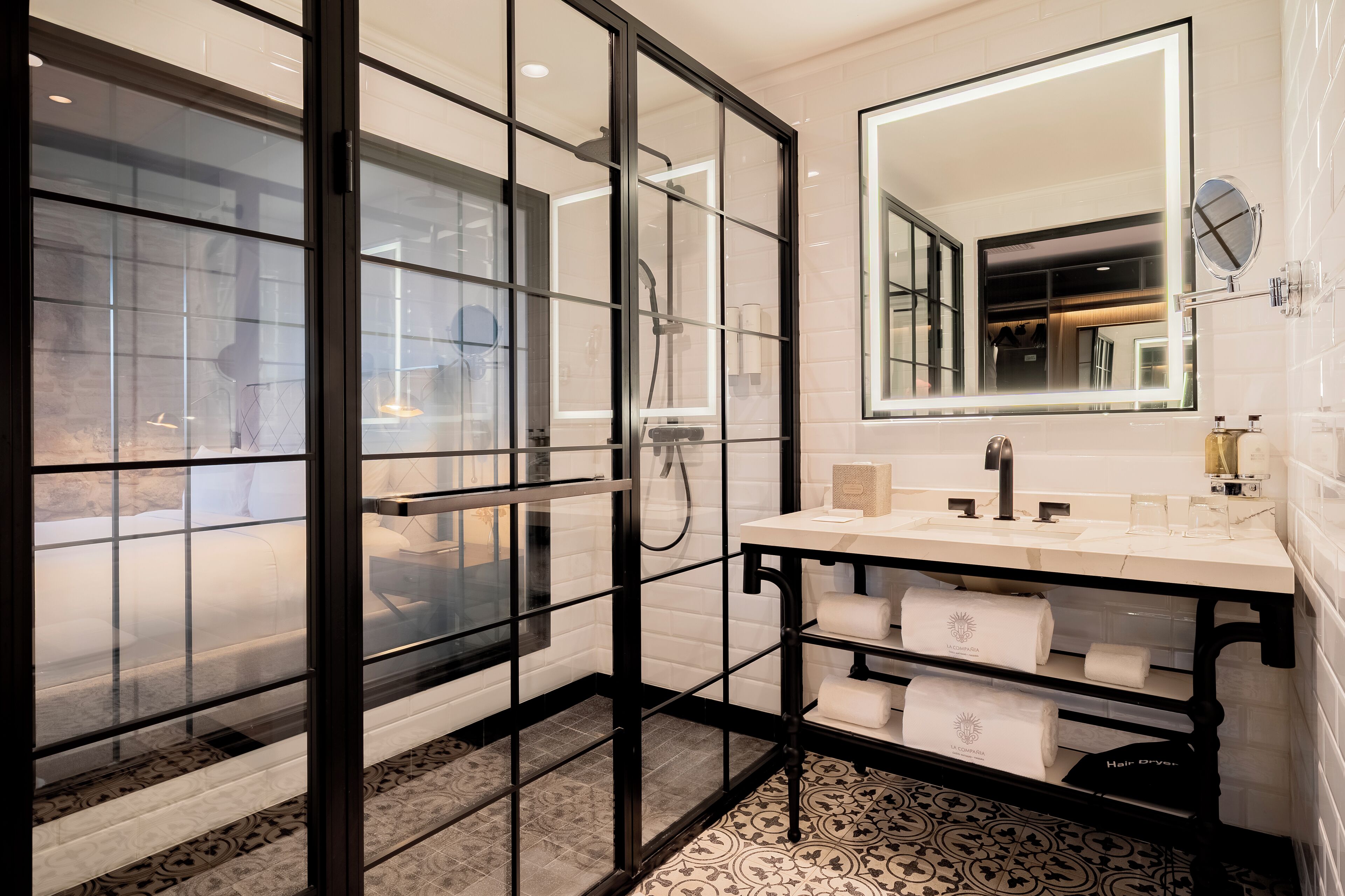 A modern bathroom with a glass-enclosed shower, a large mirror, and a vanity with multiple sinks and towel dispensers.