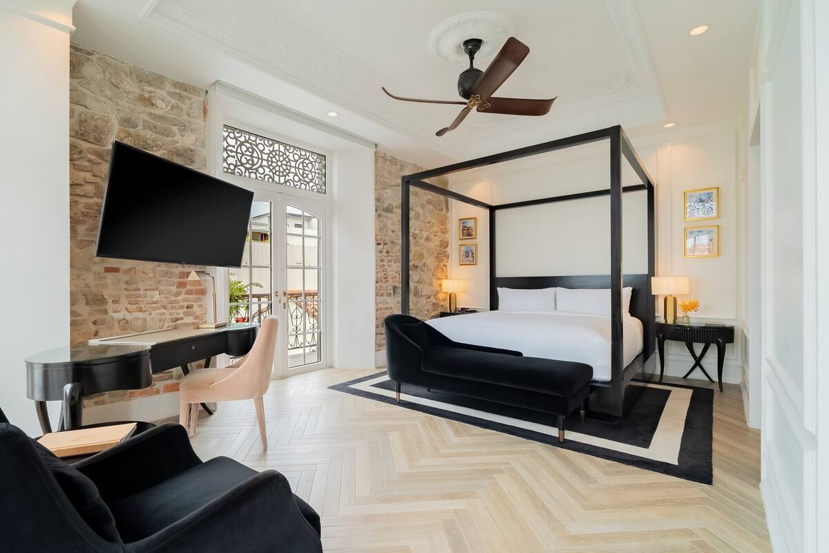 A modern hotel room with a four-poster bed, a flat-screen TV, a piano, and a dining area.