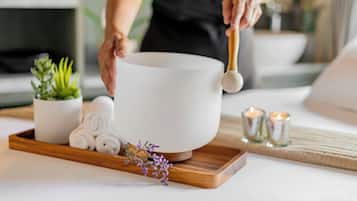 Un espace de bien-être avec un grand pot en céramique blanche, des serviettes enroulées, une plante en pot et des bougies disposées sur un plateau.