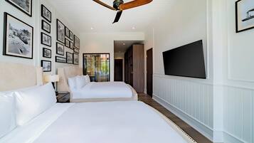 A hotel room with two beds, a ceiling fan, a TV, and framed pictures on the wall.
