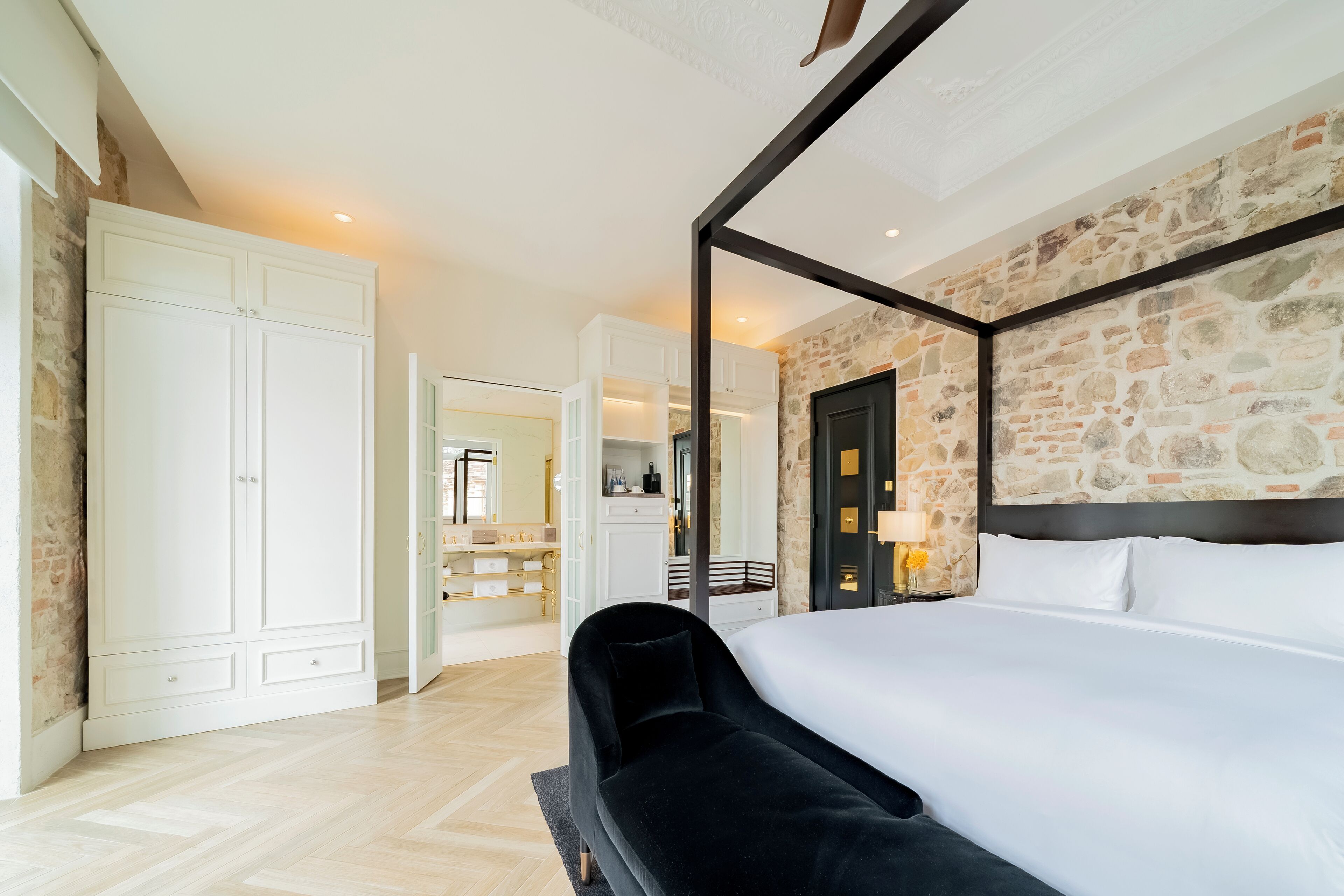 A bedroom with a large bed, a black sofa, white cabinets, and a stone wall.
