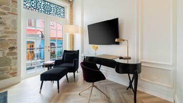 A modern hotel room with a large window, a flat-screen TV, a desk, and a comfortable seating area.