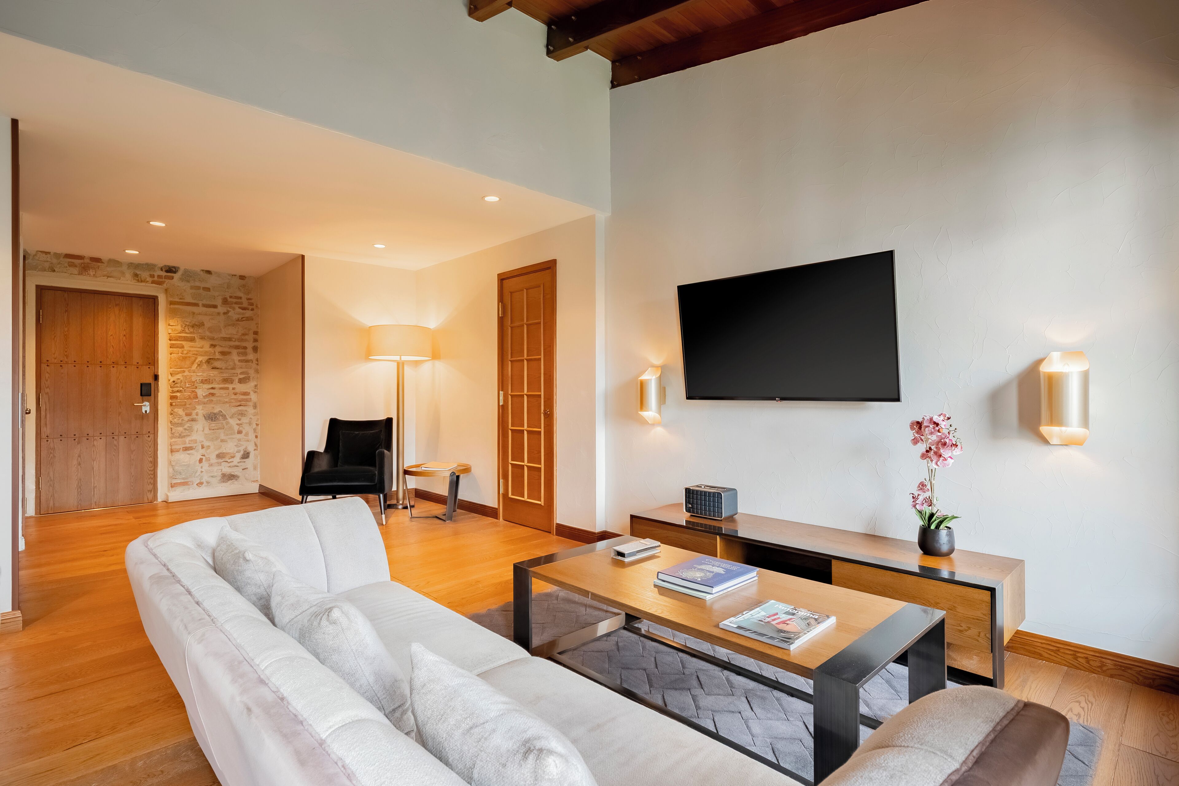 A modern living room with a sofa, coffee table, TV, and a stone wall.