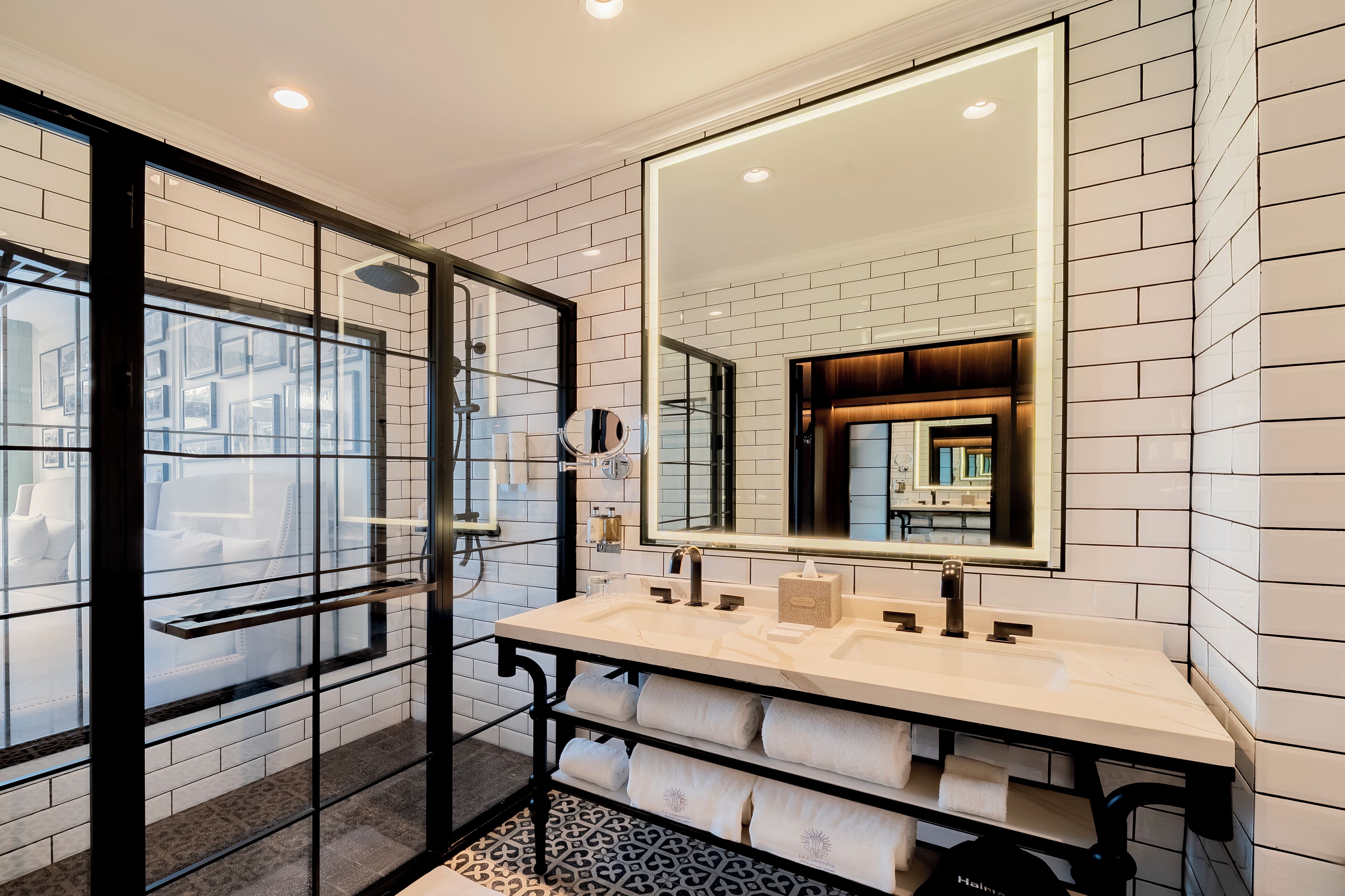 A modern bathroom with a large mirror, two sinks, and a glass shower enclosure.