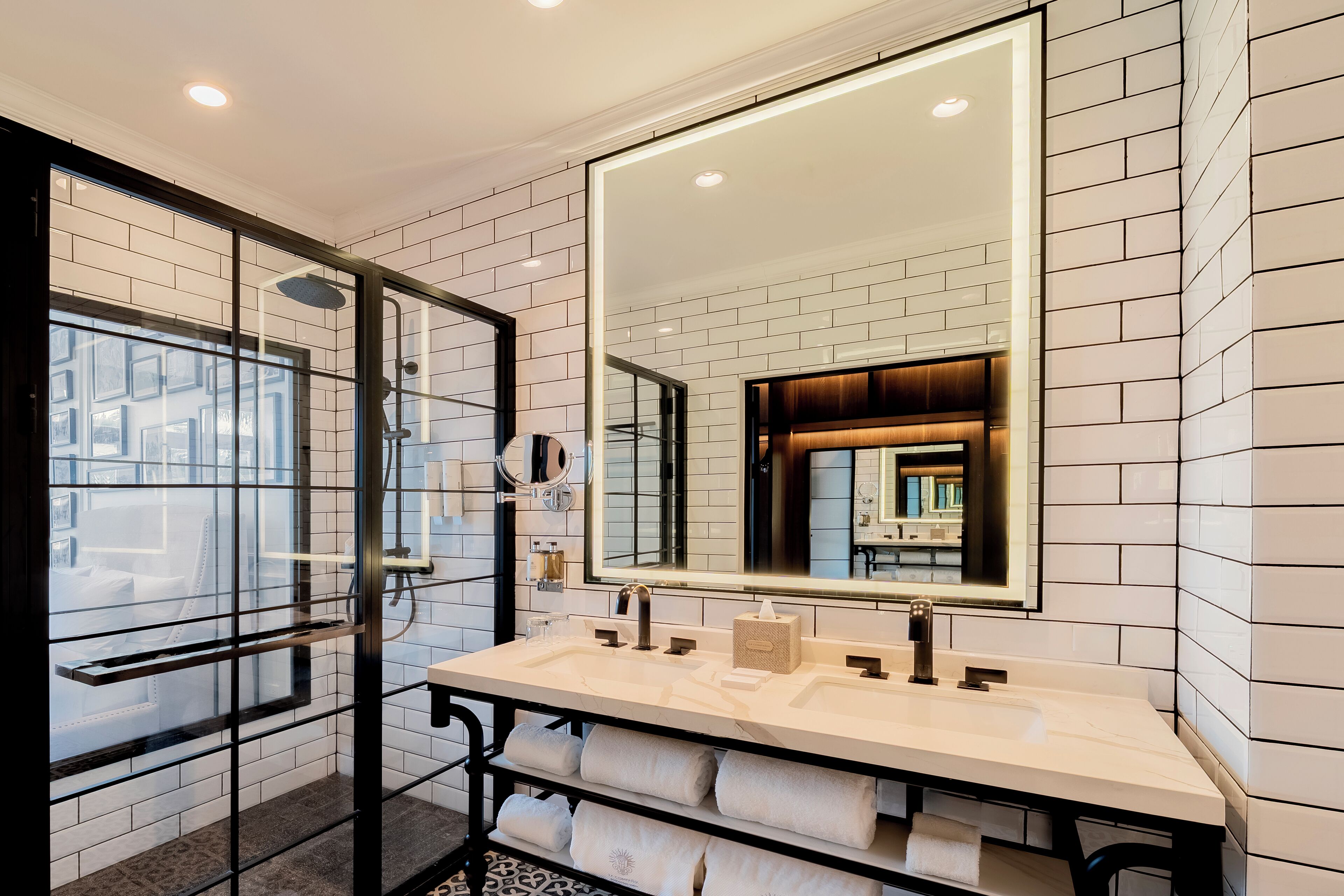 Un baño moderno con un espejo grande, dos lavamanos y una cabina de ducha de vidrio.