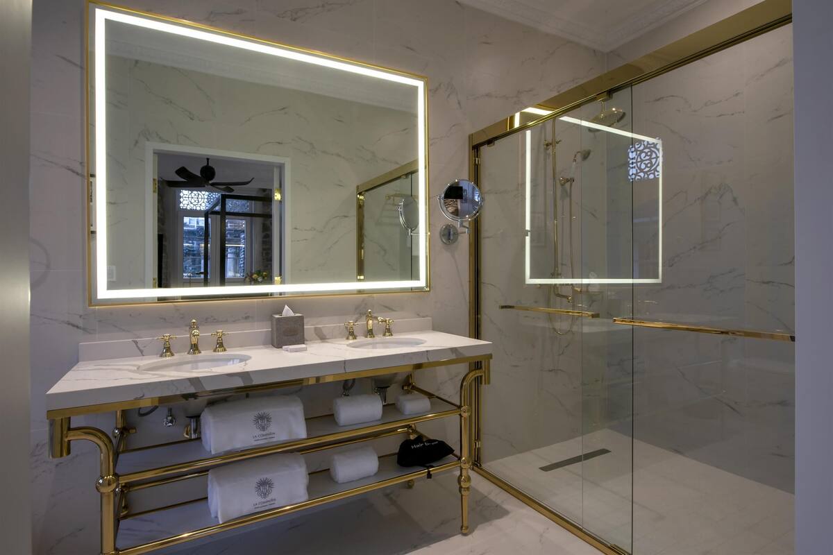 A modern bathroom with a large mirror, a glass shower enclosure, and a gold vanity.
