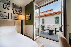 Habitación de hotel con cama, lámpara y balcón con sillas y vistas a edificios.