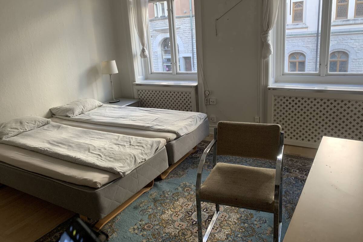 A room with two beds, a chair, a table, and a window with a view of a building.
