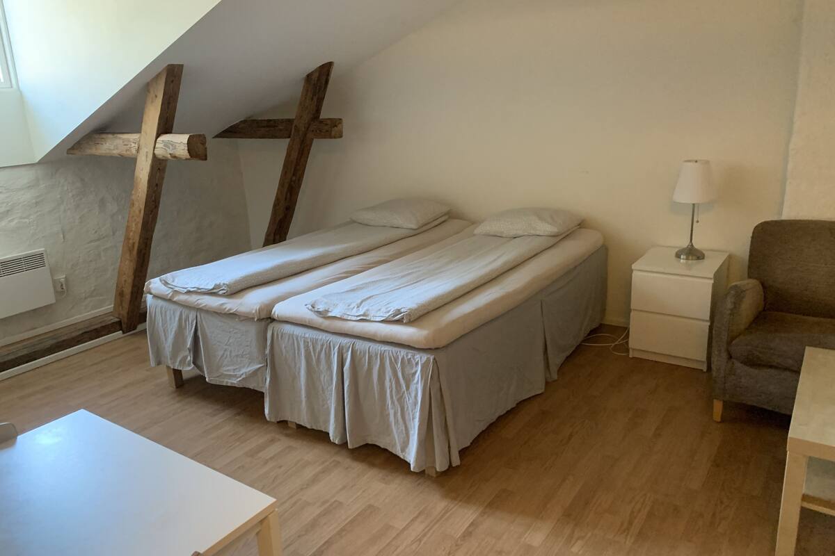A small, cozy room with a bed, a nightstand, a lamp, and a chair.