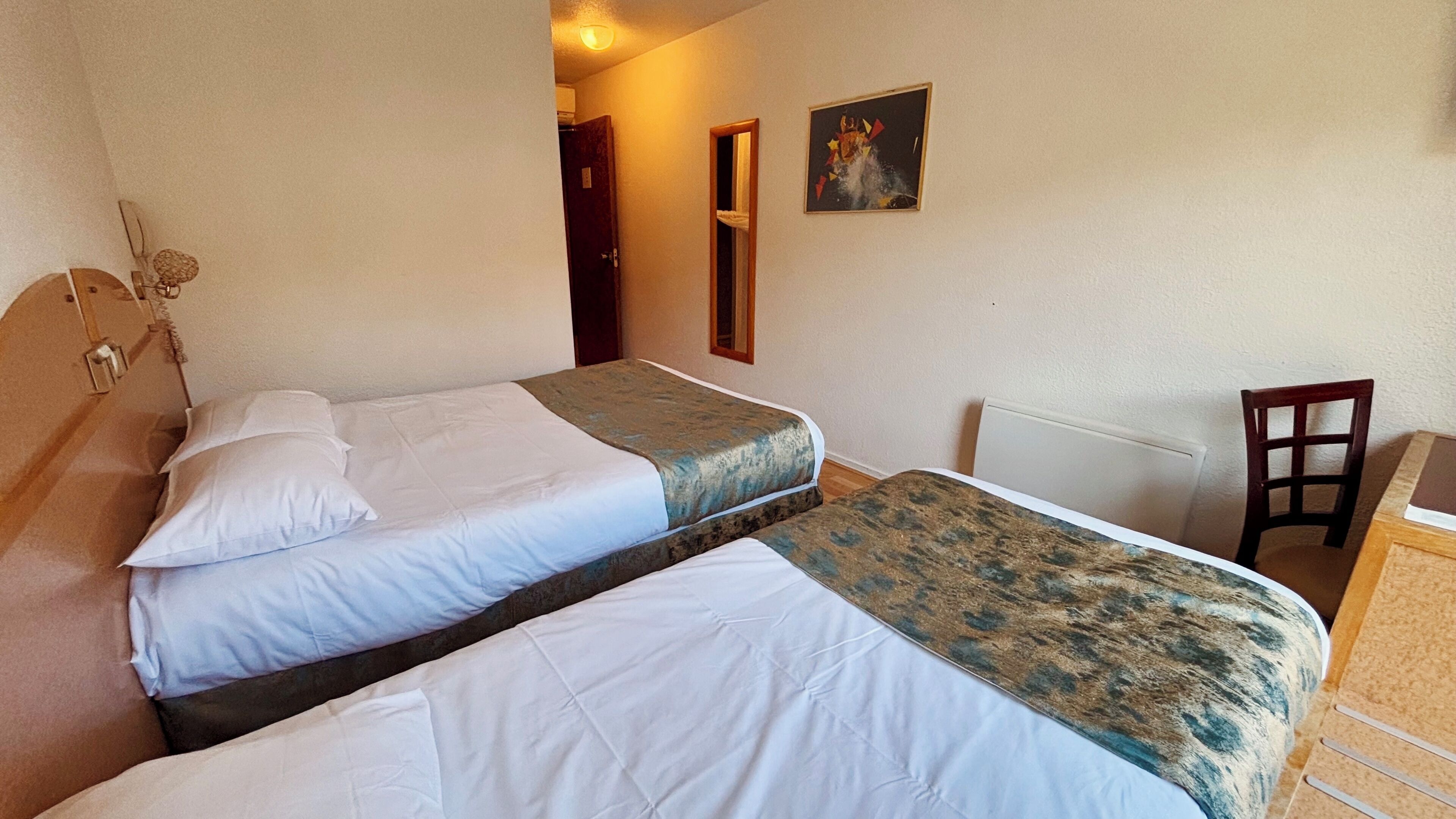 A bedroom with two beds, a wooden headboard, a chair, a radiator, and a painting on the wall.