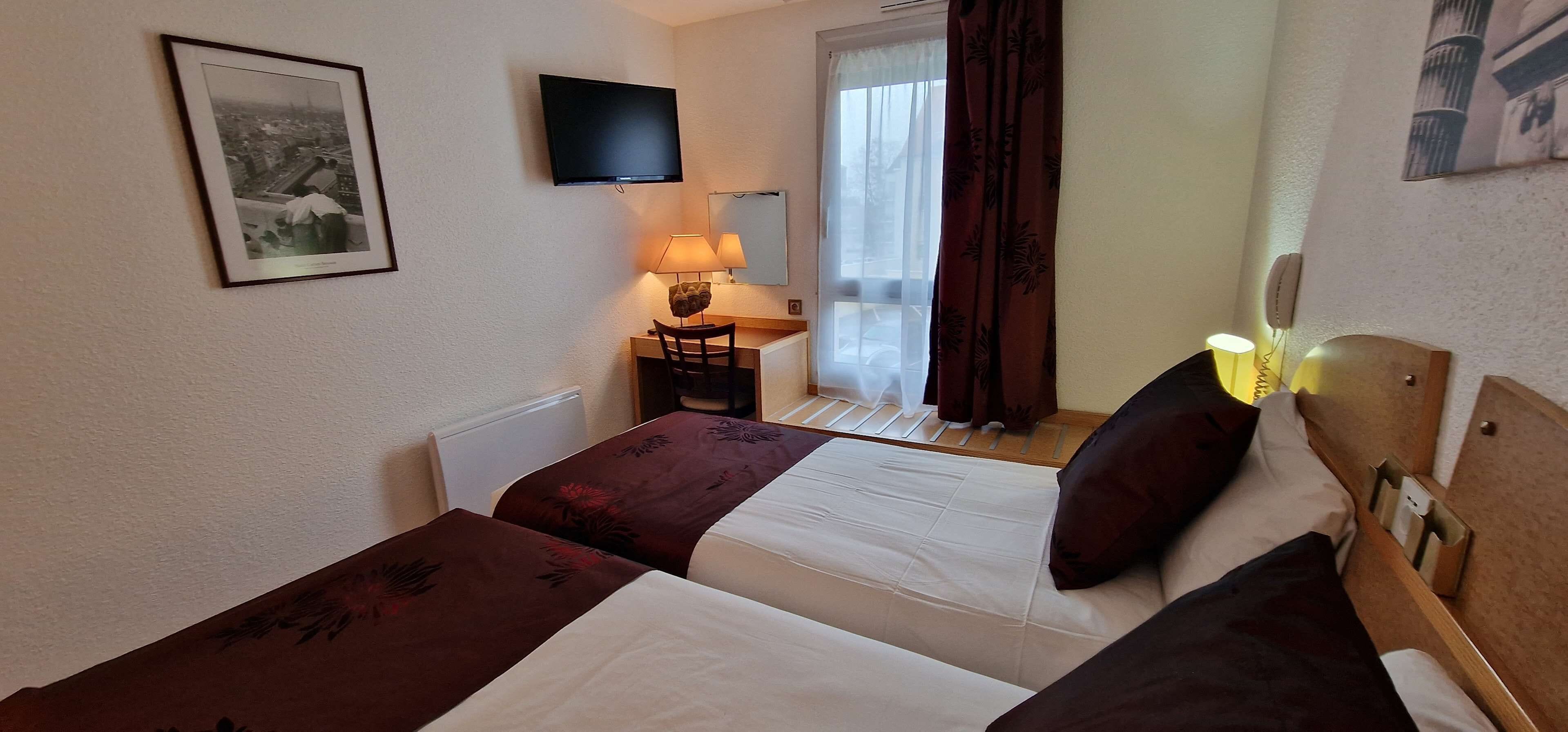 A hotel room with two beds, a desk, a chair, a lamp, a TV, and a window with curtains.