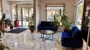 A lobby with a marble floor, blue sofas, and potted plants.
