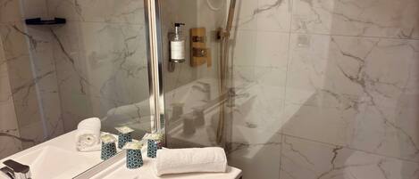 Un baño con pared de azulejos de mármol, un lavamanos blanco con grifería cromada, ducha con cerramiento de vidrio y una toalla sobre la encimera.