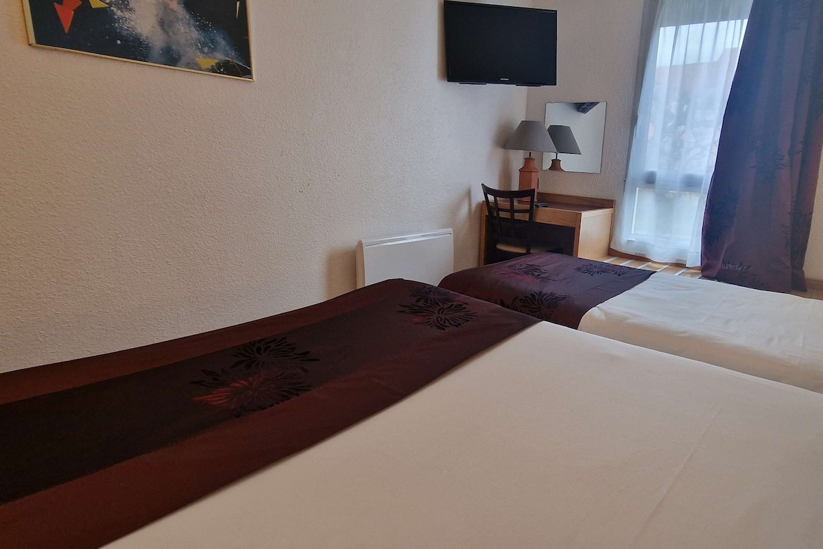 Une chambre d’hôtel avec deux lits, un bureau, une chaise, une télévision et une fenêtre avec des rideaux.