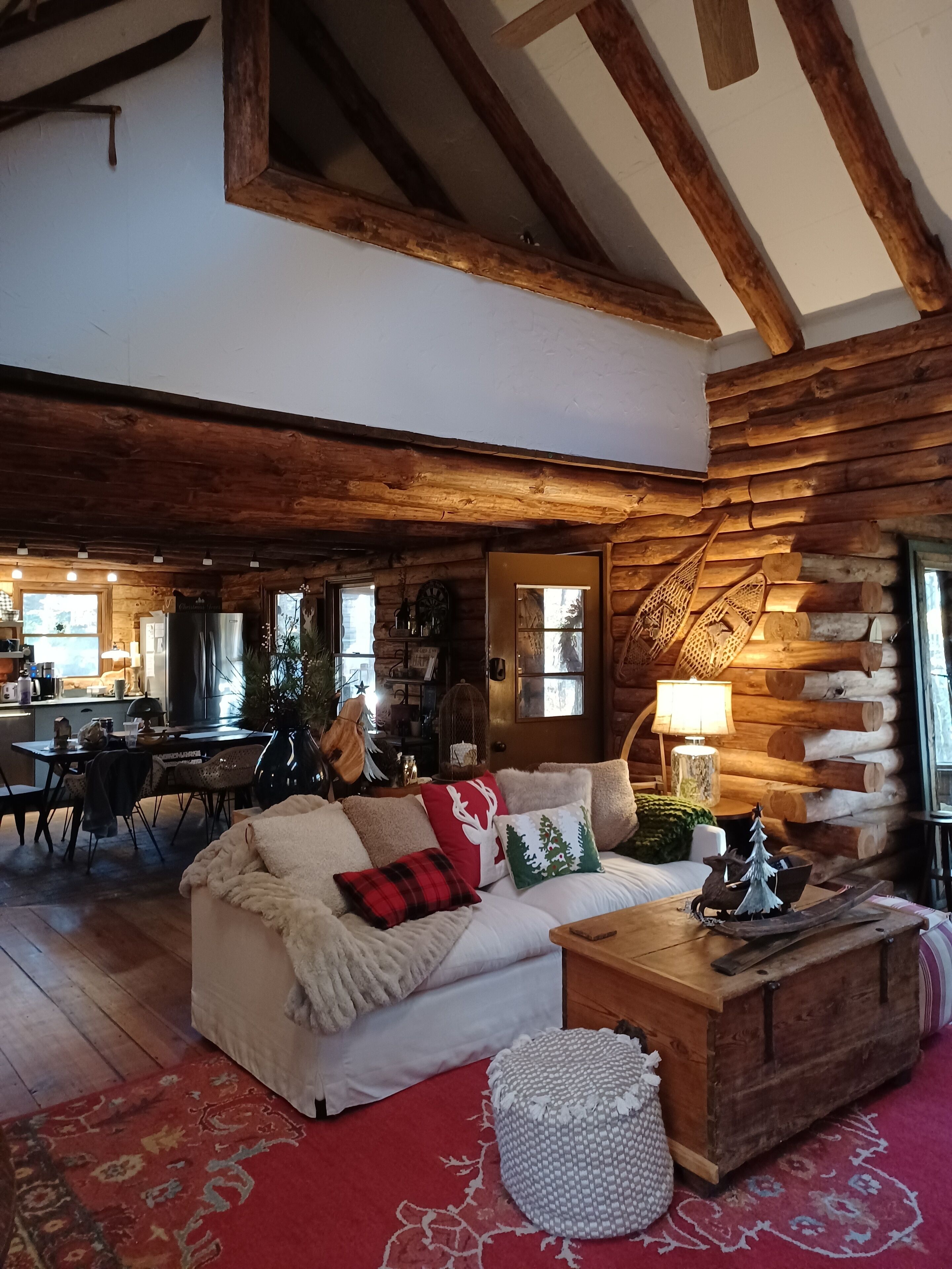 L’intérieur chaleureux d’un chalet en rondins présente un coin repas en bois, un canapé agrémenté de coussins décoratifs et un coffre en bois rustique.