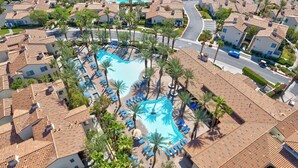 An aerial view of a resort with a central swimming pool surrounded by palm trees and lounge chairs.