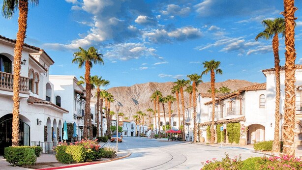 A street lined with palm trees and white buildings with balconies, under a clear blue sky.