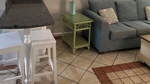 A living room with a grey sofa, a small green side table with a lamp, a white table, and a wall-mounted sign. - Right on the beach with a GREAT VIEW of the Atlantic Ocean!  Shore Drive, APATB1 (myrtle beach)