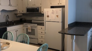 A compact kitchen with white cabinets, a microwave, a refrigerator, a sink, and a dining area with a table and chairs. - Right on the beach with a GREAT VIEW of the Atlantic Ocean!  Shore Drive, APATB1 (myrtle beach)