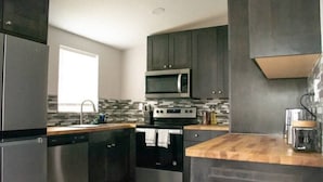 A modern kitchen with stainless steel appliances, dark cabinetry, and a wooden countertop.