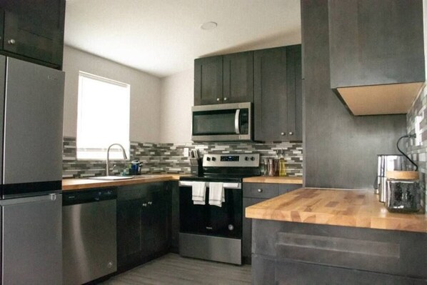 Una cocina moderna con electrodomésticos de acero inoxidable, armarios oscuros y encimera de madera.
