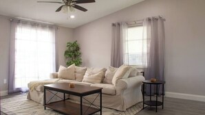 A living room with a beige sofa, a coffee table, a small side table, and a ceiling fan.