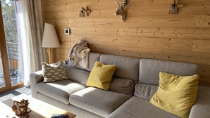 En hyggelig stue med en grå sofa, gule puder, en trævæg og et monteret dåhjortahoved.