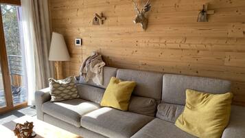 A cozy living room with a grey sofa, yellow cushions, a wooden wall, and a mounted deer head.