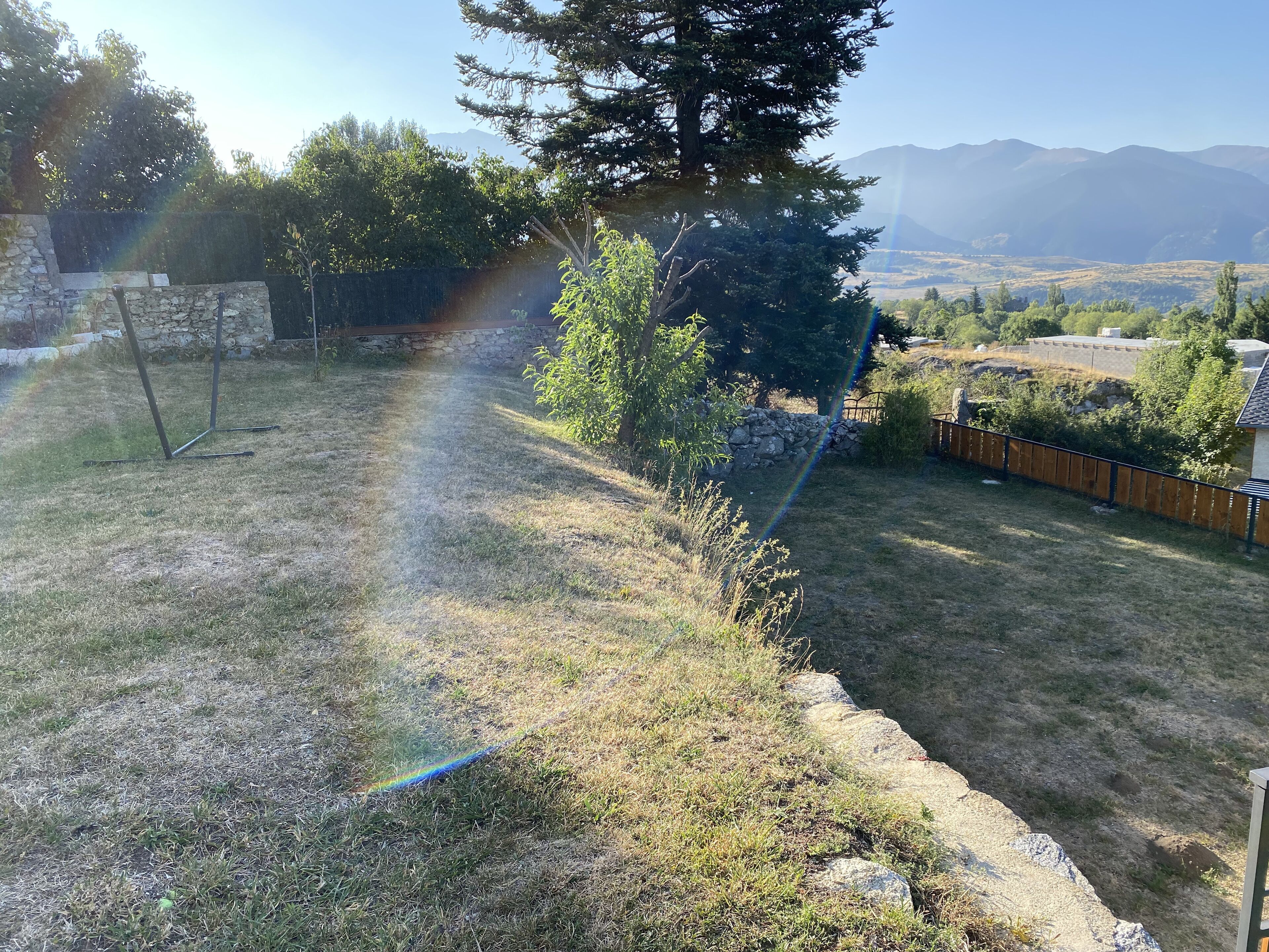 A backyard with a stone wall, a swing set, and a view of distant mountains.