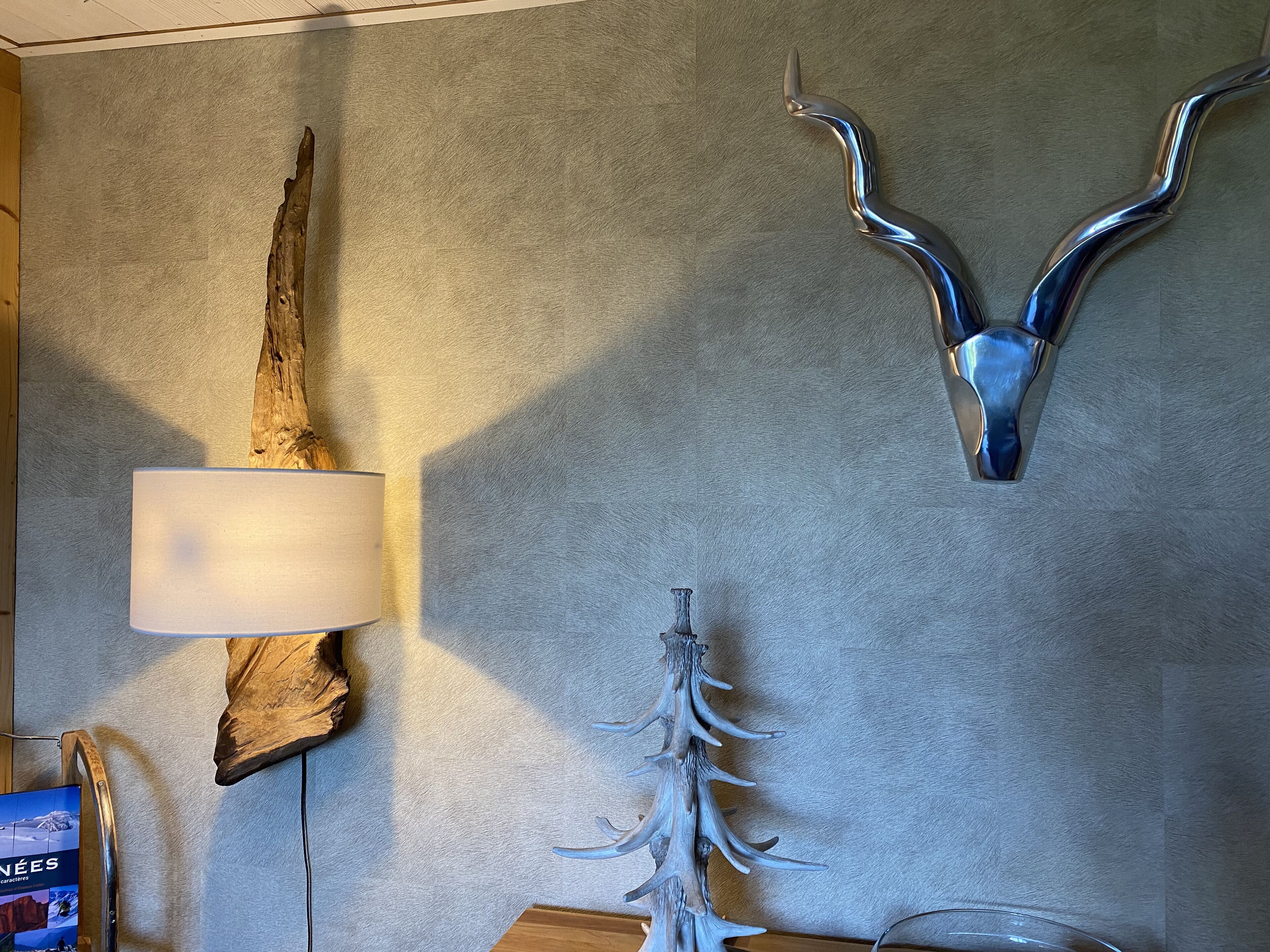 A wall with a mounted deer head, a lamp, and a wooden sculpture.