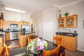 Una cocina moderna con armarios de madera, electrodomésticos de acero inoxidable y un comedor con mesa y sillas de vidrio.