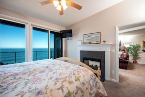 Un dormitorio con una cama grande, chimenea, televisor y vista al océano.