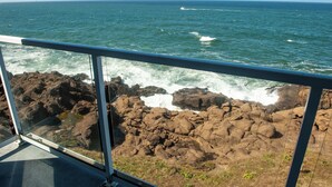 A view of the ocean from a balcony with a glass railing, rocky coastline, and waves crashing against the rocks. - Promo! Top Floor, Corner Oceanfront Condo - Indoor Pool/Hot Tub/Wifi and HDTV! (Depoe Bay)