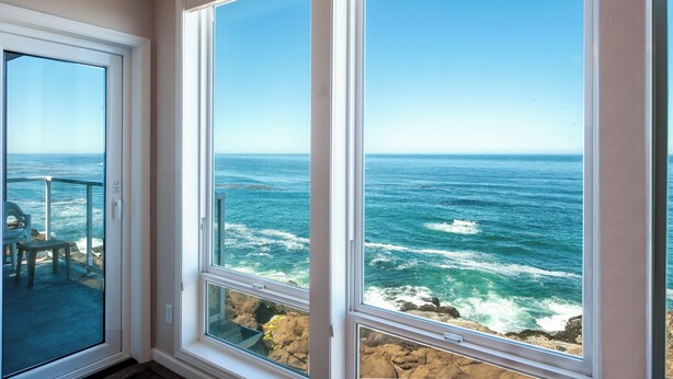 A room with large windows overlooking a rocky coastline and the ocean. - Promo! Top Floor, Corner Oceanfront Condo - Indoor Pool/Hot Tub/Wifi and HDTV! (Depoe Bay)